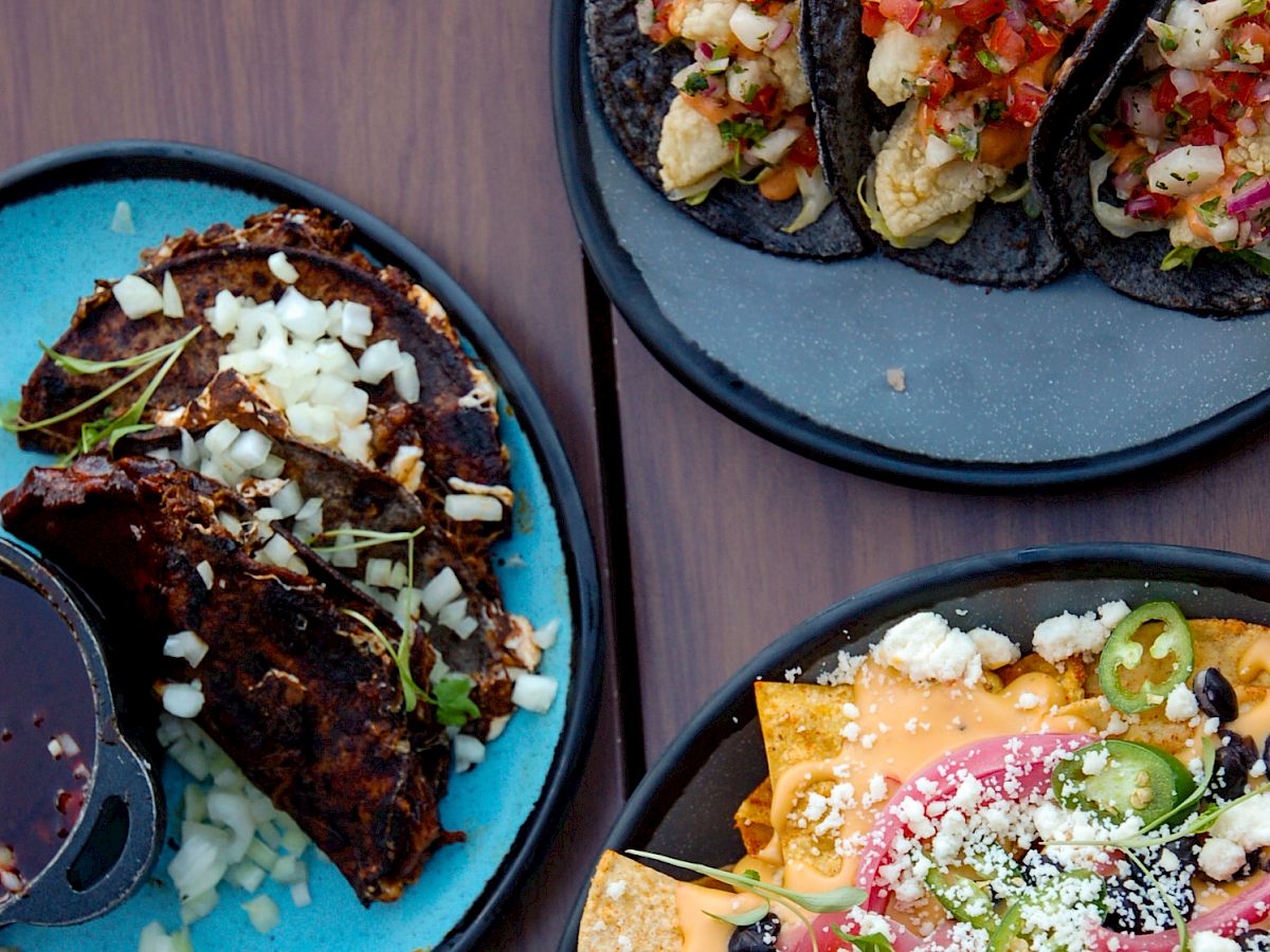 The image shows three plates of food: tacos with various toppings and a plate of nachos garnished with jalapenos, black beans, and cheese.
