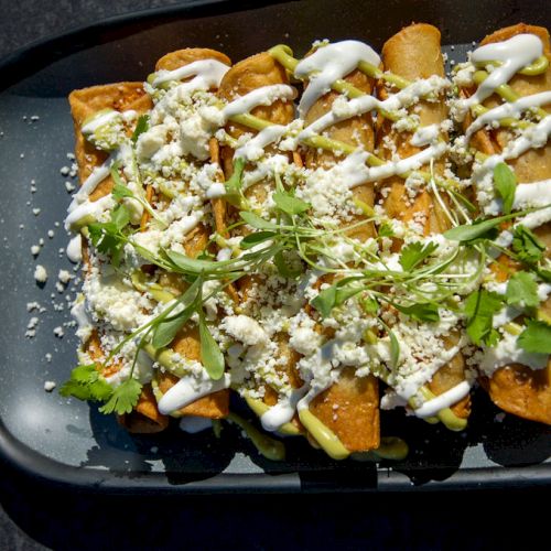 A plate of enchiladas topped with sour cream, crumbled cheese, and garnished with fresh cilantro, all served on a black tray.