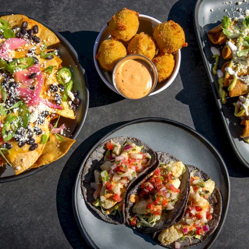 The image shows a spread of Mexican food including nachos, stuffed jalapeños, tacos, and a side of dipping sauce on a dark surface, ending the sentence.